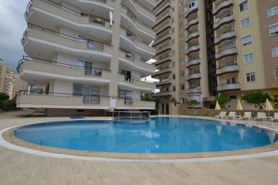 Alanya eiendom: Lyst, åpent stue- og kjøkkenområde med hvite skap, flislagt gulv og komfortable sitteplasser.