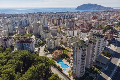 Kilátás egy alanyai ingatlanból, amely a város látképét, apartmanházakat és a Földközi-tengert mutatja be felhős ég alatt.