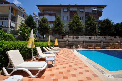 Björt stofa í Alanya með beige sófum, marmaragólfum og útsýni yfir fjöll sem sést í gegnum stóra glugga.