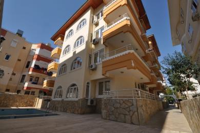Svetla, prazna soba u Alanji sa podom od terakota pločica, lučnim prozorom i toplim zidovima neutralnih tonova.