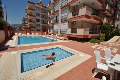 Balkon nekretnine u Alanji sa nameštajem od pruća, staklenim stolom, podom od pločica i ogradom od kovanog gvožđa, nudi svetao život na otvorenom.