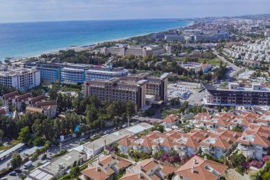 Ochiq rejadagi yorugʻ Alanya mehmonxonasi, oq divanlar, yogʻoch aksanlar va shahar manzarasi bilan.