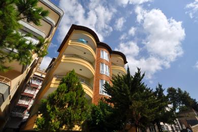 Balkon nekretnine u Alanji sa stolicama od pruća, stolom i ogradom od kovanog gvožđa sa pogledom na grad.
