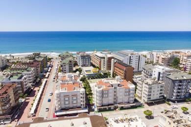 Alanya ejendom altan med hvide søjler, et glasbord og udsigt over poolen og palmerne.