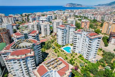 Alanya mulkidagi stol, stullar va yorqin quyosh nurida panoramali shahar va tog 'manzaralari bilan balkon.