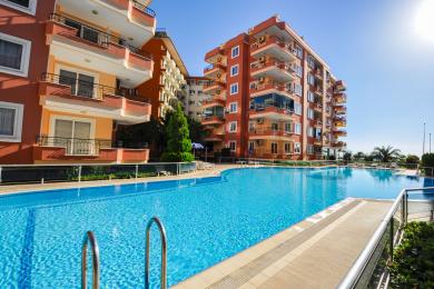 Yorug' Alanya kvartirasining qora divan, kafel pollar, ovqatlanish zonasi va balkoniga chiqish joyi bo'lgan yashash xonasi.