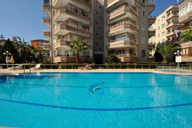 Pogled na nekretninu u Alanji koji prikazuje uređeno dvorište sa kamenim stazama i balkonima apartmana.