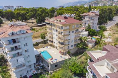 Alanya mulkidagi balkonli mehmonxona, marmar pollari, neytral divan va yorug', havodor muhit.