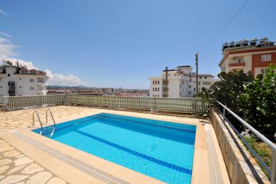 Svetli balkon u Alanji sa bež podnim pločicama, kliznim staklenim vratima i panoramskim pogledom na grad.