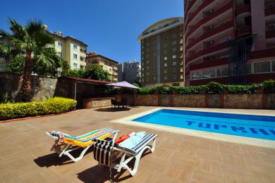 Alanya nekretnina dnevna soba s cvjetnim sofama, tamnim drvenim detaljima i svijetlom, primamljivom atmosferom.