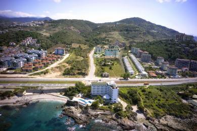 Alanya mehmonxonasi to'q qizil divan, dengiz manzarali katta derazalar va zamonaviy ovqatlanish zonasiga ega.