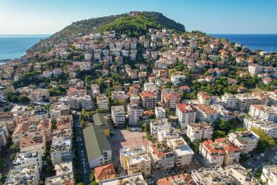 Ein sonniger Alanya-Balkon mit Rattanmöbeln bietet einen entspannenden Wohnraum im Freien und Blick auf üppiges Grün.