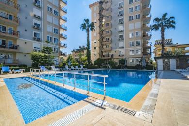 اتاق نشیمن روشن در آلانیا با مبل خنثی، صندلی راحتی، میزهای چوبی و کفپوش کاشی، فضایی دنج ایجاد می کند.