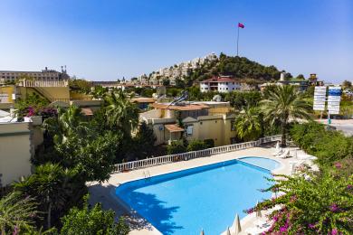Eksterijer nekretnine u Alanji: Žuta vila s balkonima, zelenim ukrasima, bujnim vrtom i sunčanom mediteranskom atmosferom.
