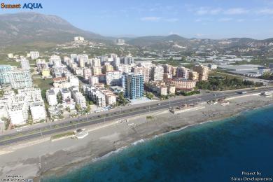 Alanya apartamentining zamonaviy yashash maydoni silliq oshxona oroli, okean manzarasi va zamonaviy osma yoritgichlarga ega.