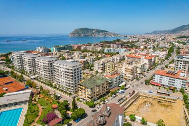 Yorqin Alanya mehmonxonasi kafel pollari, bej divan, ovqatlanish stoli va katta derazalardan tushadigan tabiiy yorug'lik bilan.