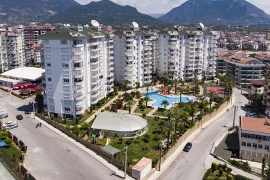 Alanya ingatlan: Világos, nyitott terű nappali bézs színű kanapéval, csempézett padlóval és modern fehér konyhával.