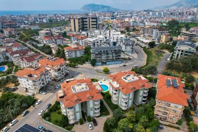 Alanya mulkidagi ochiq oshxonali, kafel pollari, neytral devorlari va qulay qizil o'rindiqlari bo'lgan yashash xonasi.