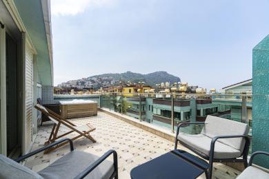 Alanya property balcony featuring a jacuzzi, tile flooring, comfortable seating, and panoramic views of the city and mountains.