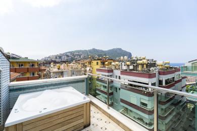 Alanya property rooftop terrace featuring a wooden-clad jacuzzi and panoramic city views under bright daylight.
