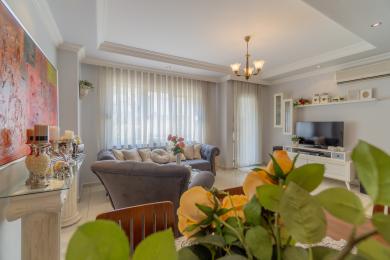 इस अलाया संपत्ति में एक आलीशान ग्रे सोफे, पारदर्शी पर्दे और एक उज्ज्वल, हवादार वातावरण के साथ एक बैठक है।