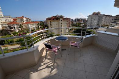 Balkon nekretnine u Alanji sa podnim pločicama, metalnom ogradom, sedištima i svetlim, sunčanim pogledom na grad.