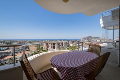 Alanya Balkon mit Holzmöbeln bietet atemberaubende Stadt- und Meerblicke unter hellem, natürlichem Licht.