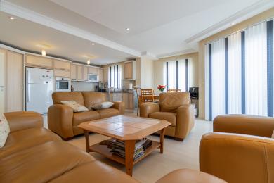 Zona de living open-space a proprietății din Alanya are canapele din piele, o bucătărie modernă și lumină naturală strălucitoare de la jaluzele verticale.