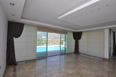 Alanya nekretnina, dnevni boravak s mramornim podovima, pogledom na bazen, ugradnom rasvjetom i elegantnim smeđim zavjesama.