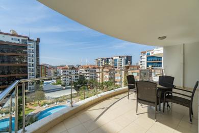 Alanya mulkidagi rattan mebellari, kafel pollari va shahar va basseynning yorqin manzarasi bilan jihozlangan balkon.