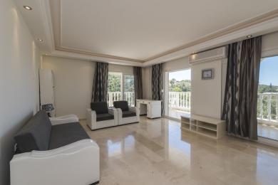 اتاق نشیمن روشن در آلانیا با کف مرمر، مبل خاکستری، دسترسی به بالکن و دکور خنثی، فضایی آرام ایجاد می کند.