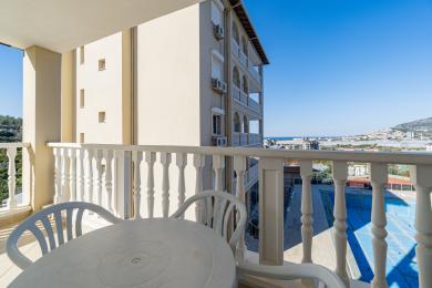 Balkon nekretnine u Alanji sa belom ogradom, plastičnim nameštajem i svetlim, sunčanim pogledom na grad.