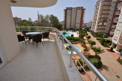Alanya mulkidagi kafel qoplamali balkon, tol mebellar va basseyn hamda obodonlashtirilgan maydonlarga qarash.