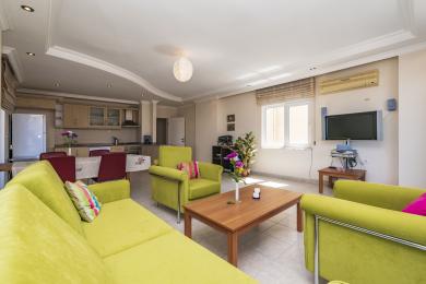 Alanya eign stofa með skærum grænum sófum, opnu eldhúsi og náttúrulegri birtu sem skapar velkomna stemningu.