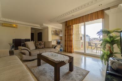 Svetlá obývacia izba v Alanyi s mramorovou podlahou, pohodlnými pohovkami a prístupom na balkón s výhľadom na mesto.