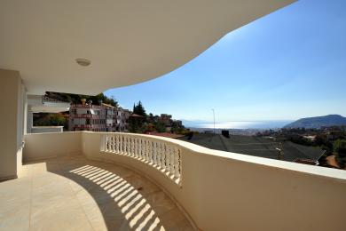 Proprietate în Alanya cu balcon cu podele de marmură, balustradă albă și vederi uimitoare la mare sub lumina puternică a soarelui.