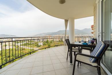 Alanya fastighet balkong med klinkergolv, rottingmöbler och panoramautsikt över bergen, vilket skapar en avkopplande atmosfär.