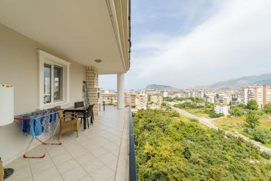 Svetli, popločani balkon u Alanji sa trpezarijom na otvorenom, roštiljem od cigle i panoramskim pogledom na grad i planine.