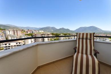 Alanyai ingatlan erkély csíkos székkel, lenyűgöző kilátást nyújt a hegyekre és a városra egy világos, napsütéses napon.