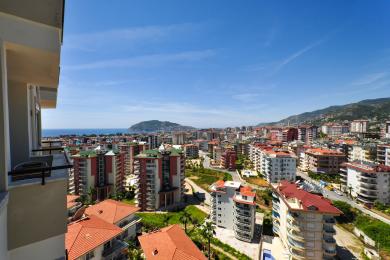 Pogled s balkona nekretnine u Alanji koji prikazuje gradski pejzaž, Sredozemno more i svijetlu, sunčanu atmosferu.