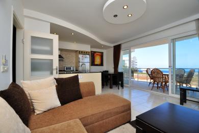 Obývacia izba apartmánu Alanya s otvorenou kuchyňou, prístupom na balkón, dlažbou a jasnou, vzdušnou atmosférou.