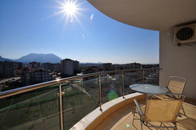 Svetli balkon u Alanji sa staklenom ogradom, prostorom za sedenje na otvorenom i panoramskim pogledom na grad i planine.