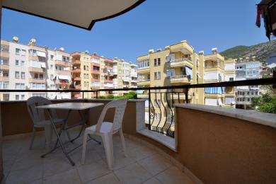 Sunčani balkon u Alanji sa podovima od pločica, belim stolom i pogledom na obližnje stambene zgrade.