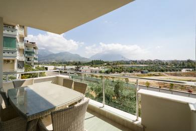 Alanya mulkidagi balkon, to‘qilgan mebellar, shisha panjaralar va yorqin, tabiiy yorug‘lik ostida tog‘ning go‘zal manzarasi.