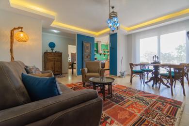 Alanya mulkidagi rang-barang gilam, ko'k aksentlar, iliq yoritish va ochiq rejadagi oshxonaga ega bo'lgan yashash xonasi qulay muhit yaratadi.