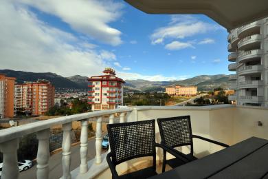 Alanya mulkidagi tog' manzarali balkon, yorqin, tabiiy yorug'likda tol stullar va marmar panjaralar bilan jihozlangan.