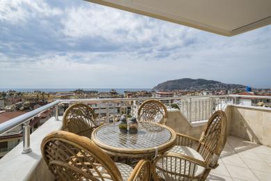 Balkon nekretnine u Alanji sa nameštajem od pruća nudi zadivljujući pogled na grad i more pod jakom, prirodnom svetlošću.