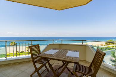 Alanya mulkidagi yog'och mebellar bilan jihozlangan balkon va yorqin, quyoshli osmon ostida ajoyib dengiz manzarasi.