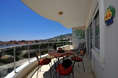 Alanya mulkidagi temir mebellar, yorqin quyosh nuri va panoramali shahar manzaralari bilan balkon.