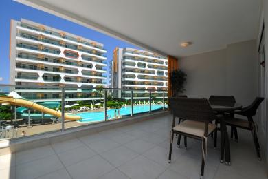 Balkon nekretnine u Alanji sa pletenim namještajem i pogledom na bazen, nudi opuštajuću i svijetlu atmosferu.